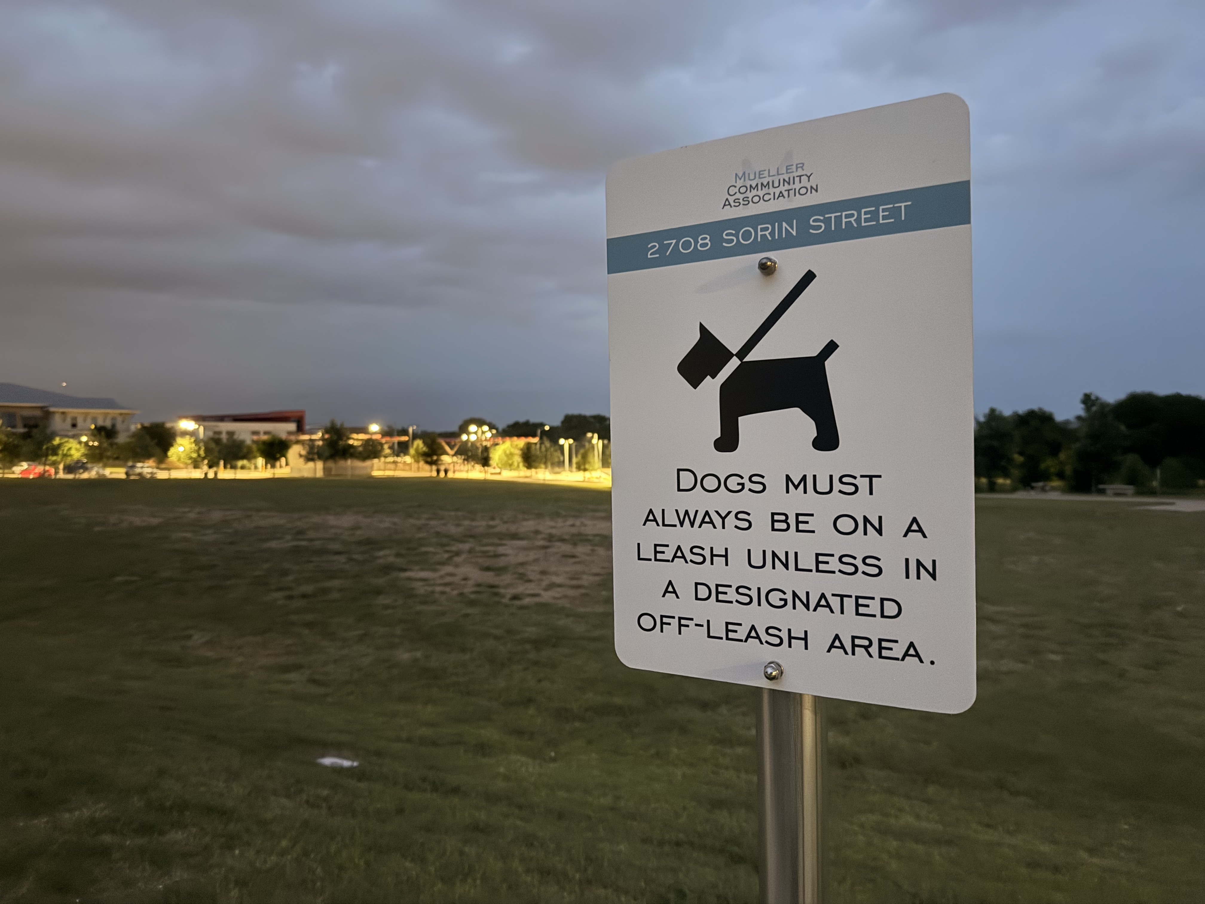 Mueller Community Association leash-required sign on Tom Miller Street at dusk